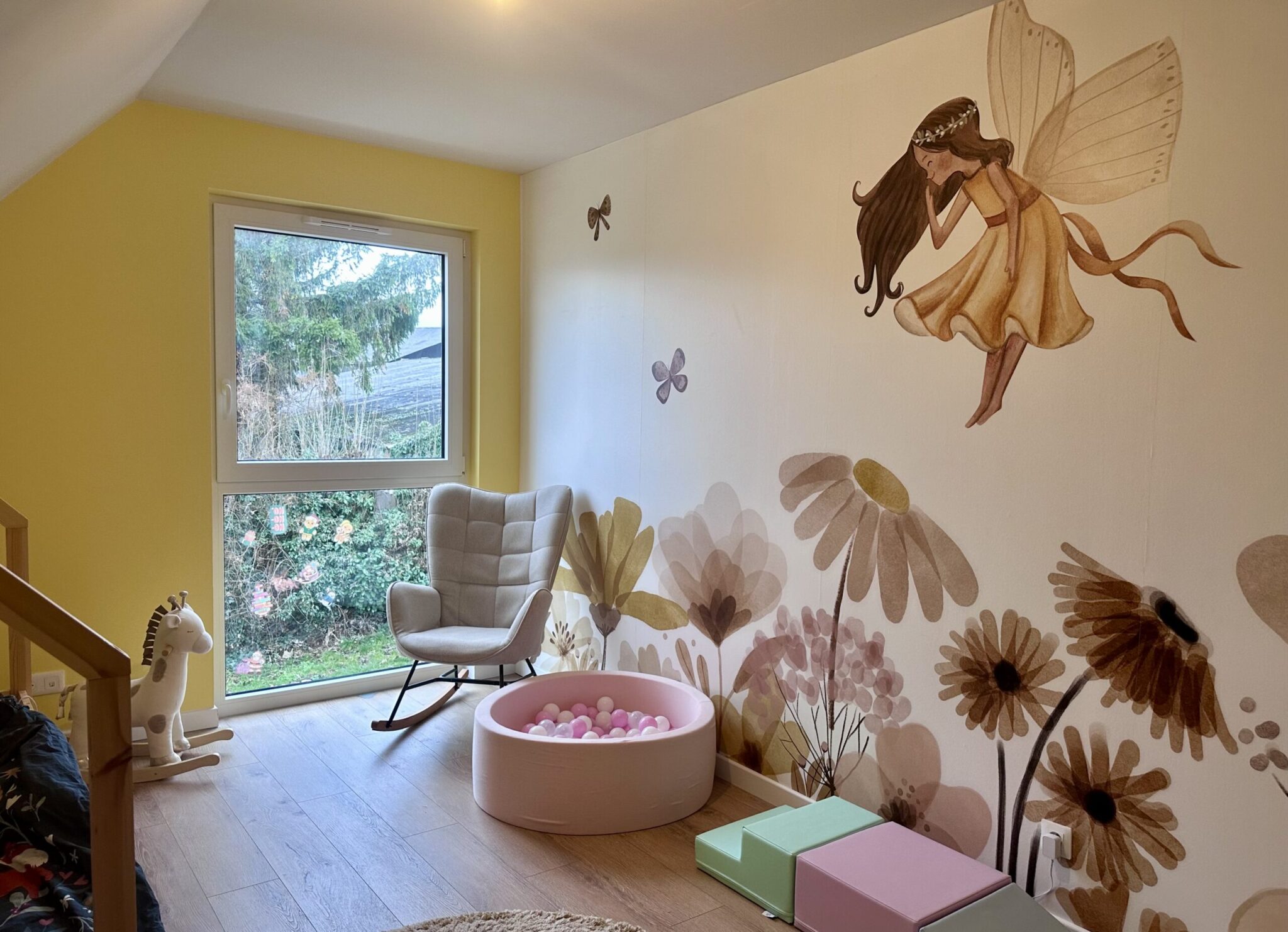 Réalisation en décoration d’intérieur d’une chambre d’enfant avec lit cabane, espace de jeux, fauteuil et mur jaune