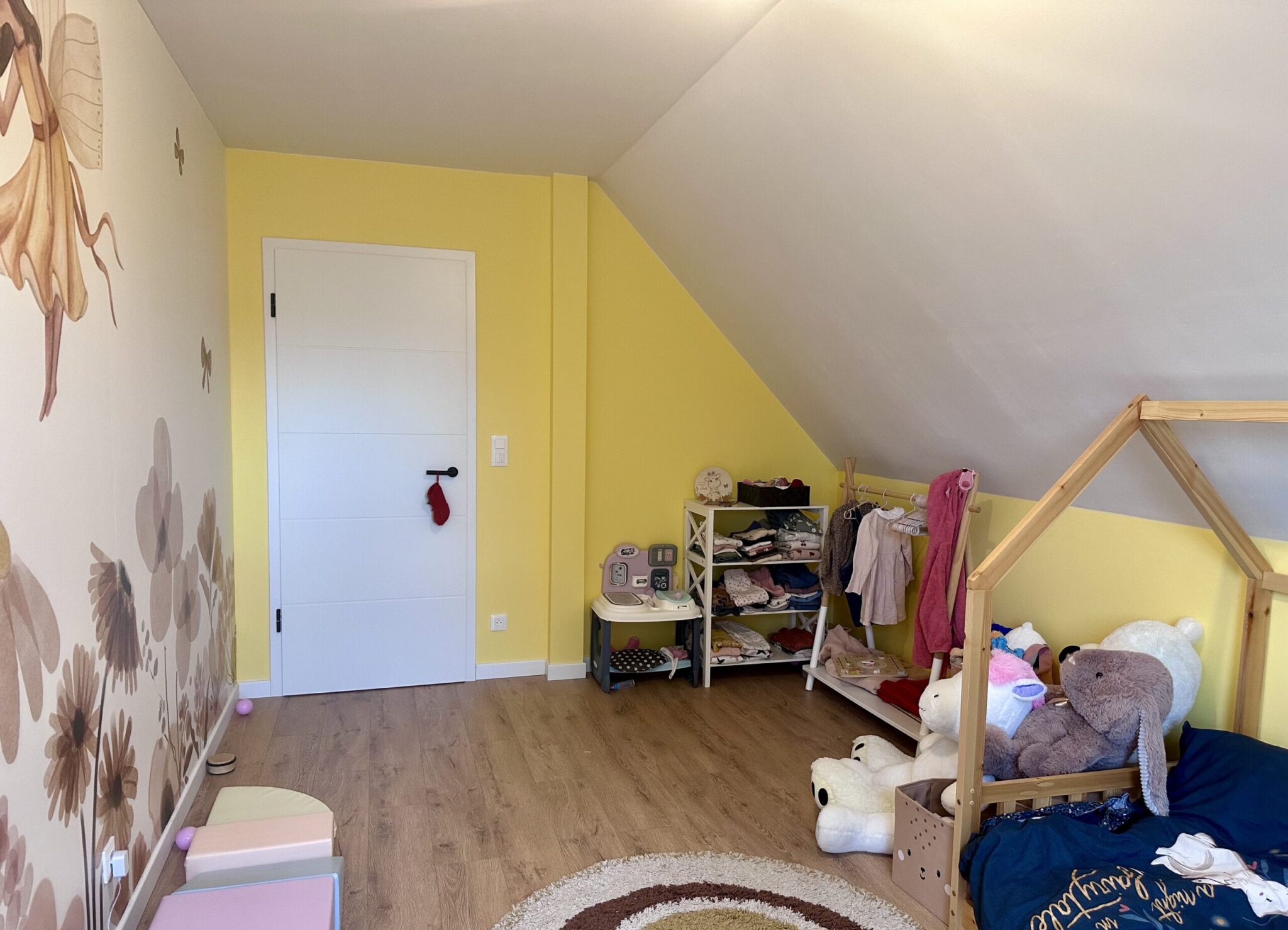 Vue générale d’une chambre d’enfant aménagée avec lit cabane, rangements accessibles, murs jaunes et sol effet bois