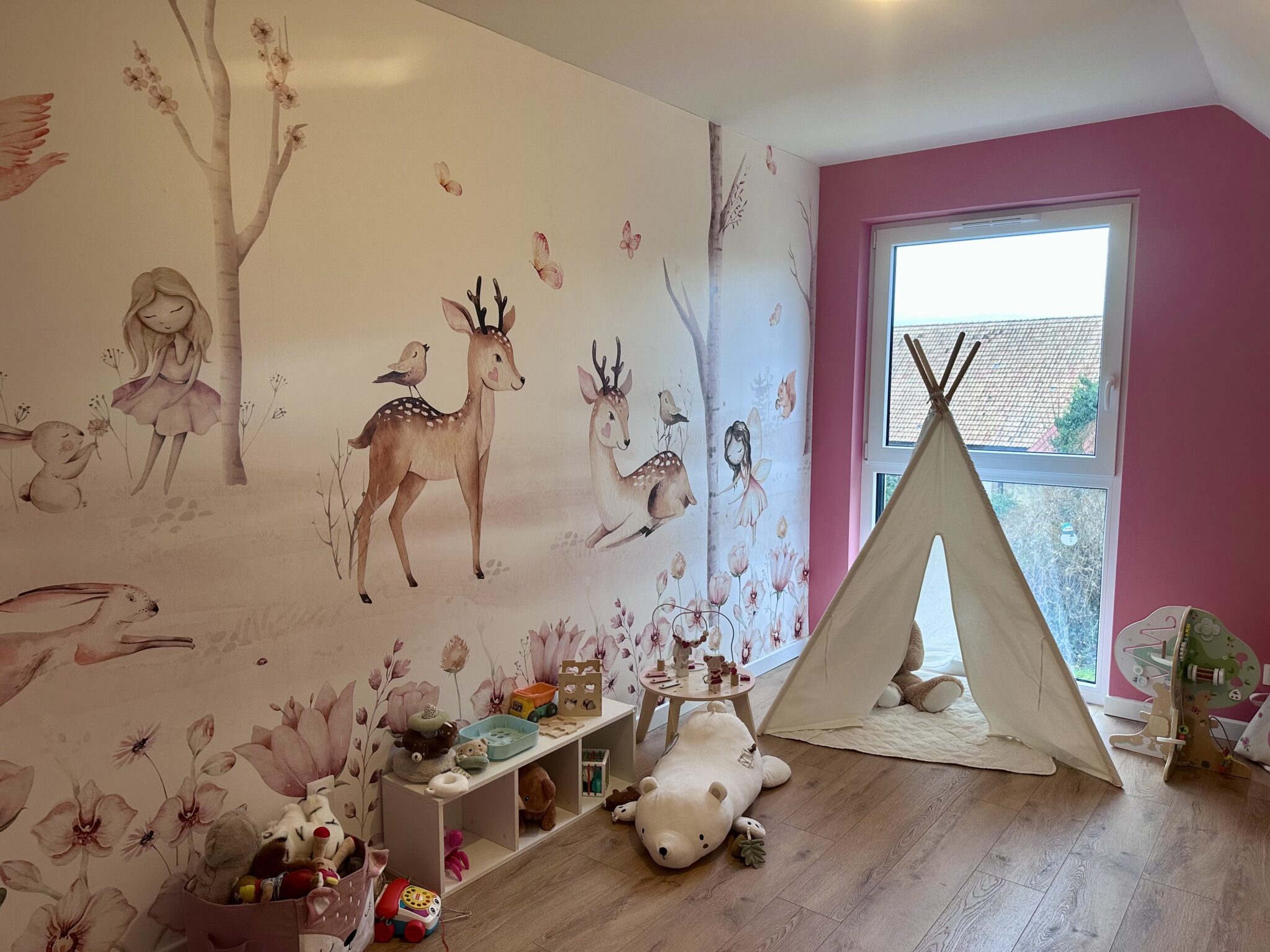 Chambre de bébé sous pente avec mur rose et papier peint représentant des animaux de la forêt