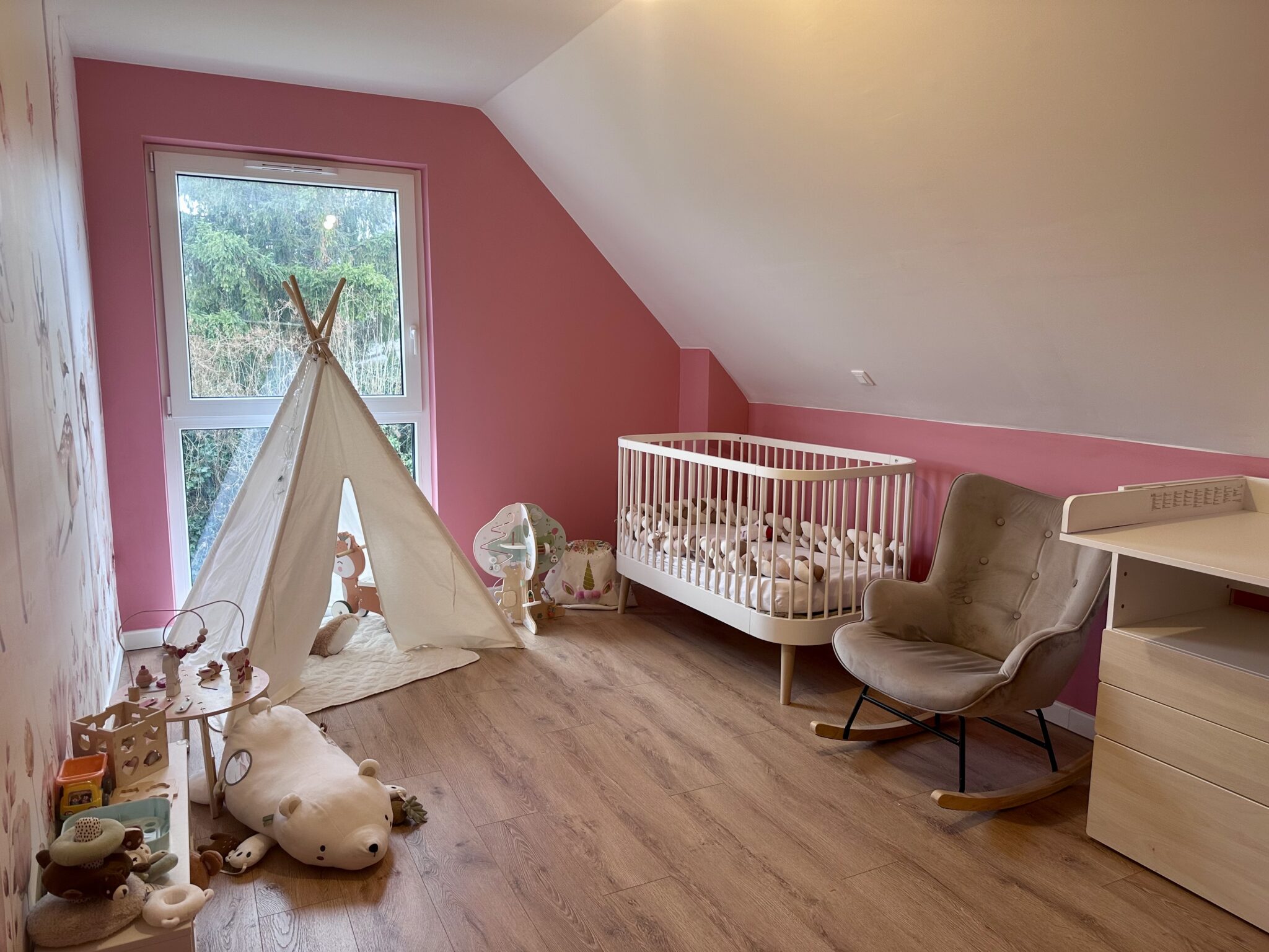 Chambre de bébé rose aménagée avec un lit à barreaux, un tipi et un fauteuil à bascule