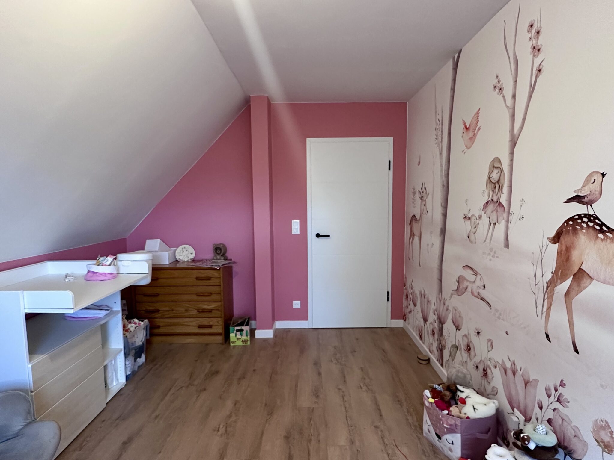 Chambre de bébé sous pente avec mur rose et papier peint représentant des animaux de la forêt