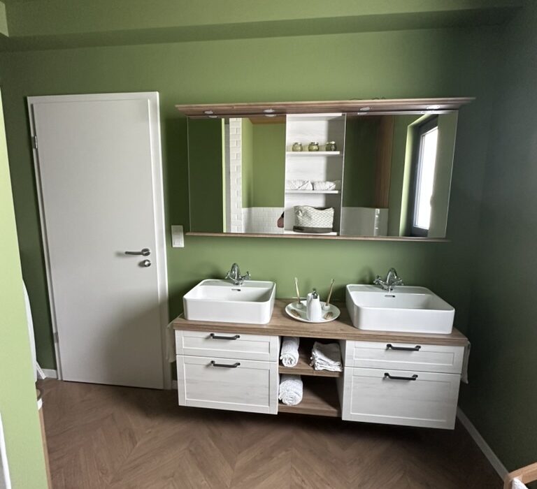 Réalisation en architecture d’intérieur d’une salle de bain verte avec meuble double vasque et sol effet parquet en chevrons